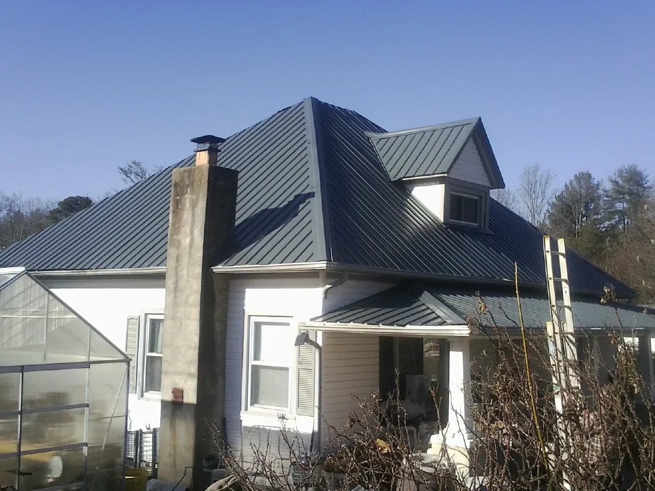 Dark blue standing seam metal roof on a white farmhouse with dormer — Slate & Tile Roof Repair by Roofing Brothers in Glendora